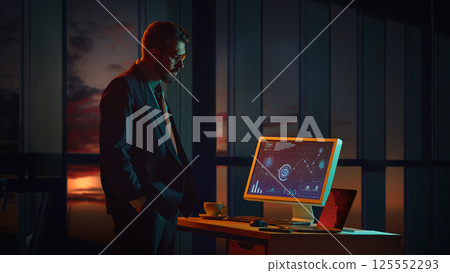 Businessman standing in his office late at night, looking at economic data on computer screen. Negative trend, bankruptcy. 125552293