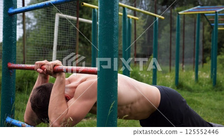 Young muscular athlete doing exercise on triceps at sport equipment outdoor. Male shirtless athlete working out at sport ground. Strong sporty man training at nature. Concept of healthy lifestyle 125552446