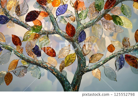 Colorful glass tree sculpture shines against a bright blue sky with white clouds during daylight hours 125552798