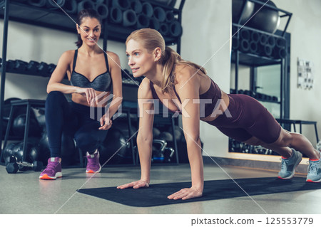 Coach in the gym working with a customer and both looking involved 125553779