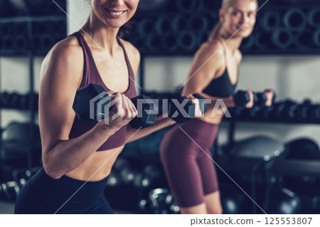 Two young caucasian women exercising with dumbbells and looking focused 125553807