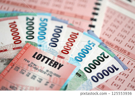 Red lottery ticket lies on pink gambling sheets with indonesian rupiah money bills. Lottery playing concept or gambling addiction in indonesia Red lottery ticket lies on pink gambling sheets with indonesian rupiah money bills. Lottery playing concept or gambling addiction in indonesia 125553936
