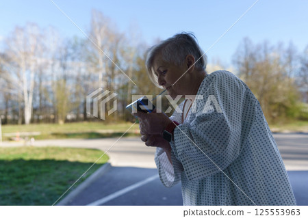 Female patient in hospital gown smoking outside a medical facility. 125553963