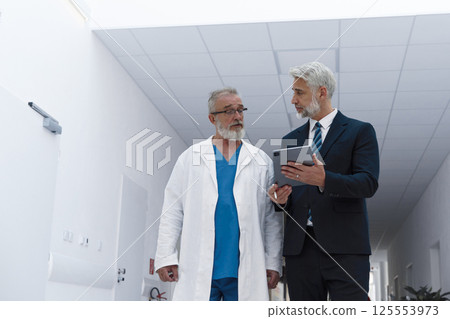 Doctor talking with hospital manager, walking down hospital hallway. 125553973