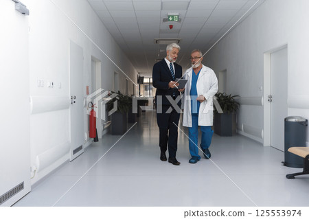 Doctor talking with hospital manager, walking down hospital hallway. 125553974