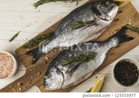Fresh dorado fish with lemon, rosemary and spices on wooden cutting board, close up 125553977