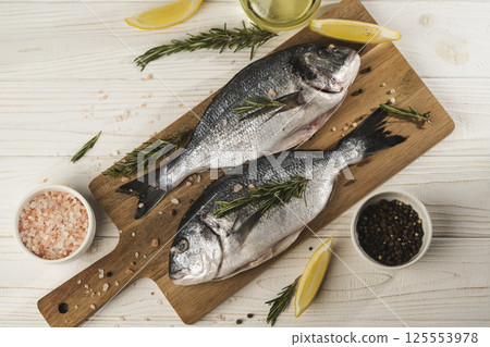 Fresh dorado fish with lemon, rosemary and spices on wooden cutting board, close up Fresh dorado fish with lemon, rosemary and spices on wooden cutting board, close up 125553978