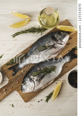 Fresh dorado fish with lemon, rosemary and spices on wooden cutting board, close up 125553979