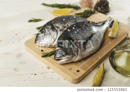 Fresh dorado fish with lemon, rosemary and spices on wooden cutting board, close up Fresh dorado fish with lemon, rosemary and spices on wooden cutting board, close up 125553983