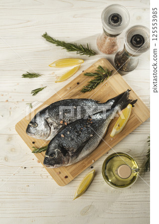Fresh dorado fish with lemon, rosemary and spices on wooden cutting board, close up 125553985