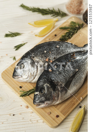 Fresh dorado fish with lemon, rosemary and spices on wooden cutting board, close up 125553987