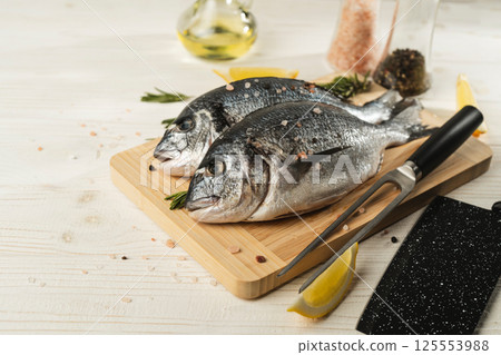 Fresh dorado fish with lemon, rosemary and spices on wooden cutting board, close up 125553988