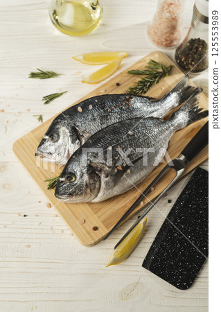 Fresh dorado fish with lemon, rosemary and spices on wooden cutting board, close up 125553989