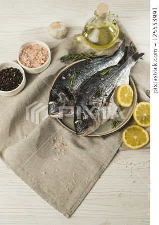 Fresh dorado fish with lemon, rosemary and spices on a plate, close up Fresh dorado fish with lemon, rosemary and spices on a plate, close up 125553991