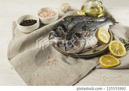 Fresh dorado fish with lemon, rosemary and spices on a plate, close up Fresh dorado fish with lemon, rosemary and spices on a plate, close up 125553992