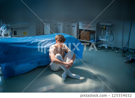 Worried teenage patient sitting alone on hospital floor, struggling with mental health issues. 125554032