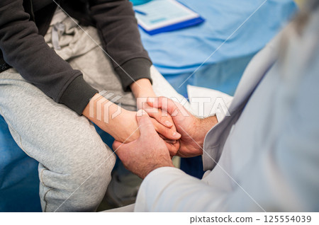 Close up of compassionate doctor holding hands of anxious teenage patient before surgery. Close up of compassionate doctor holding hands of anxious teenage patient before surgery. 125554039