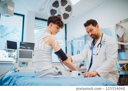 Teen boy undergoing medical checkup with doctor in hospital room. 125554048