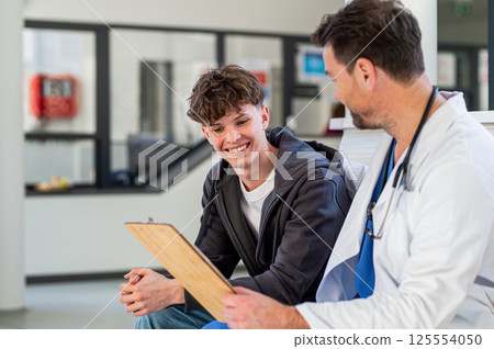 Teenage boy smiling talking with doctor, receiving positive health news. 125554050