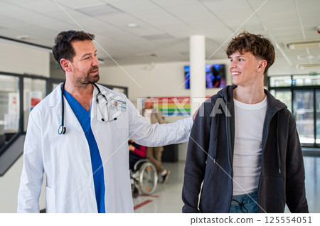 Doctor walking with teenage patient after successful medical procedure in hospital. 125554051