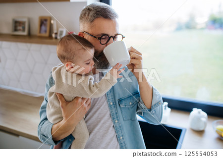Father holding baby son in arms and drinking coffee. Father holding baby son in arms and drinking coffee. 125554053