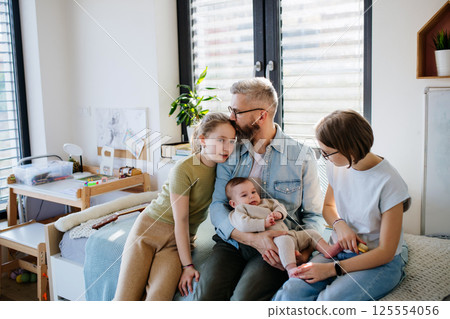 Three sisters looking at newborn brother in fathers arms. 125554056