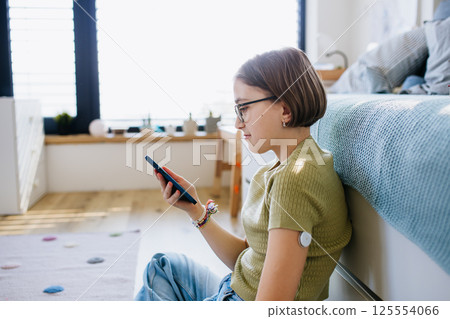 Diabetic girl with CGM sensor checking her blood sugar in app. 125554066