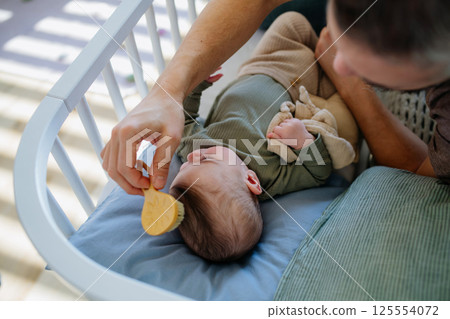 Father putting the baby to sleep, lying next to him in the crib. 125554072