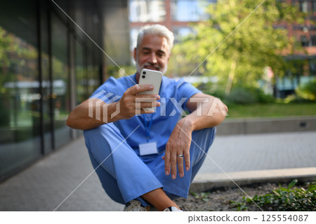 Healthcare worker outside hospital and checking phone during break. 125554087