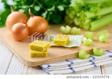 chicken bouillon cubes and fresh vegetables for soup on white wooden table, selective focus. chicken bouillon cubes and fresh vegetables for soup on white wooden table, selective focus. 125554774