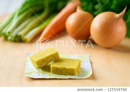 chicken bouillon cubes and fresh vegetables for soup on white wooden table, selective focus. chicken bouillon cubes and fresh vegetables for soup on white wooden table, selective focus. 125554780