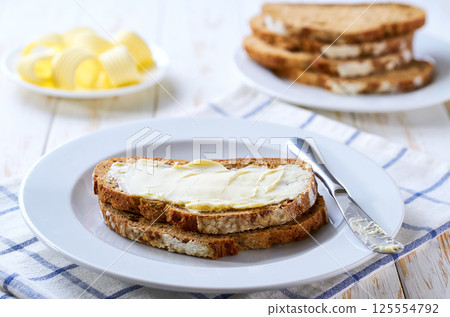 spreading butter on to crusty rye bread slices on a white wooden table. spreading butter on to crusty rye bread slices on a white wooden table. 125554792