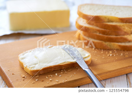 Tasty cut wheat bread  with fresh butter on a white wooden table. 125554796