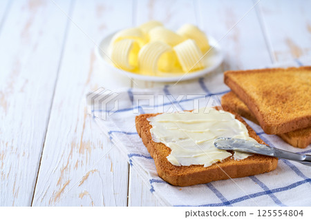 spread butter on a golden crispy pieces of toast on a cutting board, selective focus. spread butter on a golden crispy pieces of toast on a cutting board, selective focus. 125554804