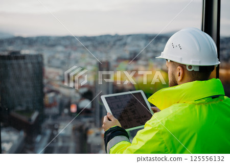 Rear view of construction site manager using digital tablet to inspect building progress. Rear view of construction site manager using digital tablet to inspect building progress. 125556132