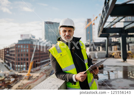 Engineer checking building documentation on clipboard at construction site. Engineer checking building documentation on clipboard at construction site. 125556143