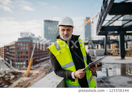 Engineer checking building documentation on clipboard at construction site. Engineer checking building documentation on clipboard at construction site. 125556144