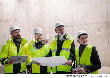 Team of engineers and construction workers reviewing blueprints, building site. 125556167