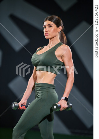 determined woman stands confidently in fitness center lifting dumbbells. She wears stylish workout attire and showcases her strength and dedication health and fitness. determined woman stands confidently in fitness center lifting dumbbells. She wears stylish workout attire and showcases her strength and dedication health and fitness. 125556423