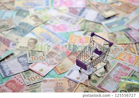 Supermarket trolley on many banknotes of different currency. Background of shopping worldwide Supermarket trolley on many banknotes of different currency. Background of shopping worldwide 125556727
