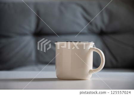 White mug on white table at home interior in living room. Beverage. Mockup. Perfect for businesses selling mugs, overlay your design on to image. White mug on white table at home interior in living room. Beverage. Mockup. Perfect for businesses selling mugs, overlay your design on to image. 125557024