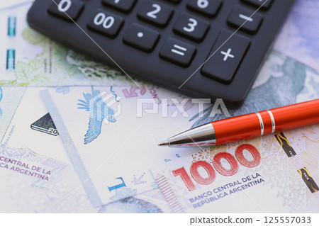 Argentine pesos money bills in big amount lies on table with pen and calculator close up 125557033