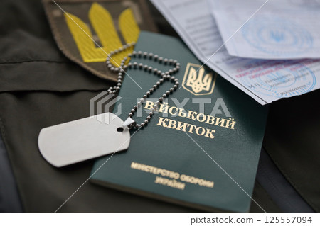 Military token or army ID ticket with mobilization notice lies on green ukrainian military uniform 125557094