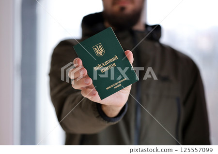 Young ukrainian conscript soldier shows his military token or army ID ticket indoors 125557099