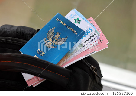 Blue Republic Indonesia passport with money and airline tickets on touristic backpack 125557100