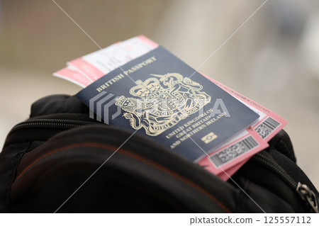 Blue British passport with airline tickets on touristic backpack Blue British passport with airline tickets on touristic backpack 125557112