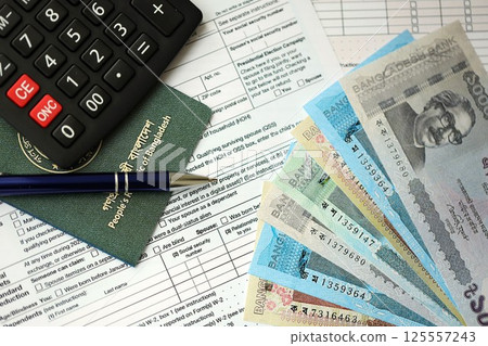 Bangladeshi taka money bills lies on table with pen, calculator, passport and tax forms Bangladeshi taka money bills lies on table with pen, calculator, passport and tax forms 125557243