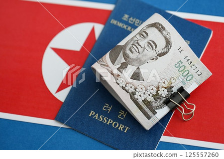 North Korean won money bills in big amount and passport lies on People Republic of Korea flag 125557260