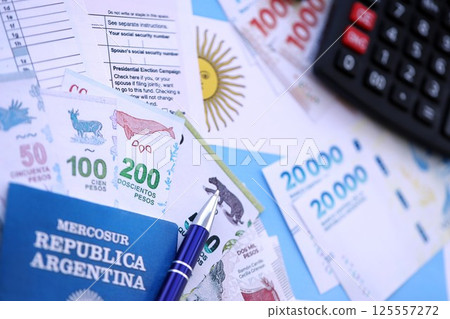 Argentine pesos money bills in big amount lies on table with pen, calculator, passport and tax forms 125557272