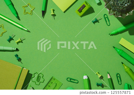 A frame of bright green stationery. Pens, pencils, markers, clipboards, pins, notepad, sharpener, sticky notes, eraser, ruler. Space for your text. 125557871